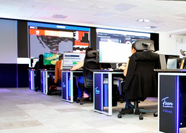 Fila de estaciones de trabajo del NOC con paneles de marca Ferrer & Asociados y analistas monitoreando pantallas de mapas y datos